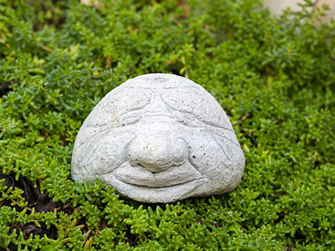 Grinsender Beton-Kopf im Blumenbeet